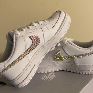 May include: White leather low-top sneakers with a jeweled Nike swoosh and the text "NIKE AIR" on the side.
