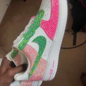 May include: White leather sneakers with a pink and green rhinestone design. The word "AIR" is written in pink on the side of the shoe.