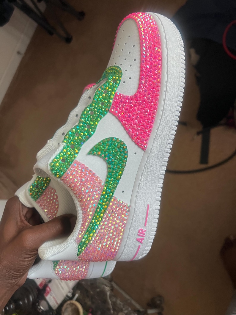 May include: White leather sneakers with a pink and green rhinestone design. The word "AIR" is written in pink on the side of the shoe.