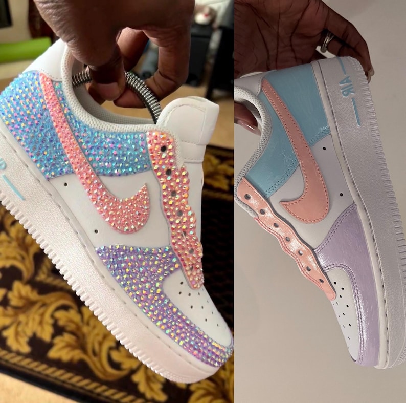 May include: Two pairs of white sneakers with colorful designs. One pair has a pink, blue, and purple design with rhinestones. The other pair has a light blue, pink, and purple design. Both pairs say "AIR" on the side.