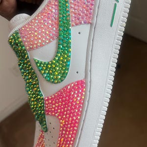 May include: White low-top sneakers with a green and pink rhinestone design. The word "AIR" is printed on the side of the shoe.