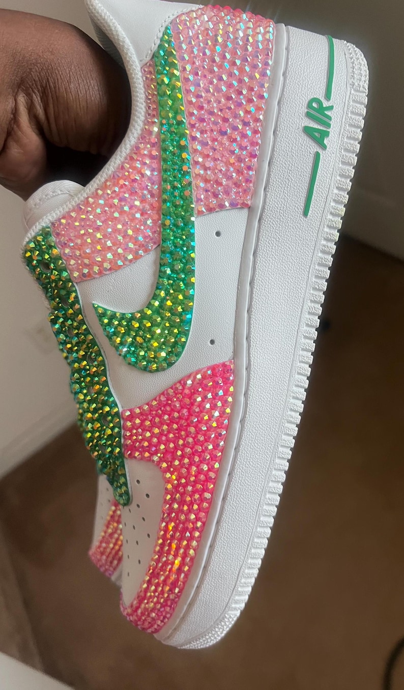 May include: White low-top sneakers with a green and pink rhinestone design. The word "AIR" is printed on the side of the shoe.