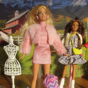 May include: Two fashion dolls with long blonde and brown hair wearing pink and yellow outfits. The dolls are standing on a white stand with a white dress form. The dolls are holding pink and blue dresses.
