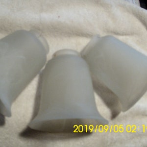 May include: Three frosted glass bell-shaped light shades. The shades are a soft white color and have a flared bottom. The image is taken on a white surface. The date and time stamp is visible in the image.