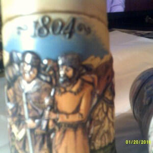 May include: A ceramic stein with a blue and white background featuring a scene of three men in period clothing. The stein has the year "1804" written on the front.