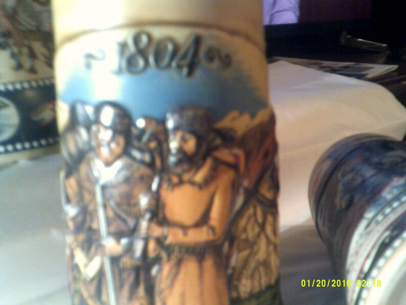 May include: A ceramic stein with a blue and white background featuring a scene of three men in period clothing. The stein has the year "1804" written on the front.
