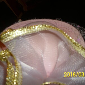 May include: A pink hat with a gold trim and white tulle. The hat has a date, 2018/03/10, written on it.