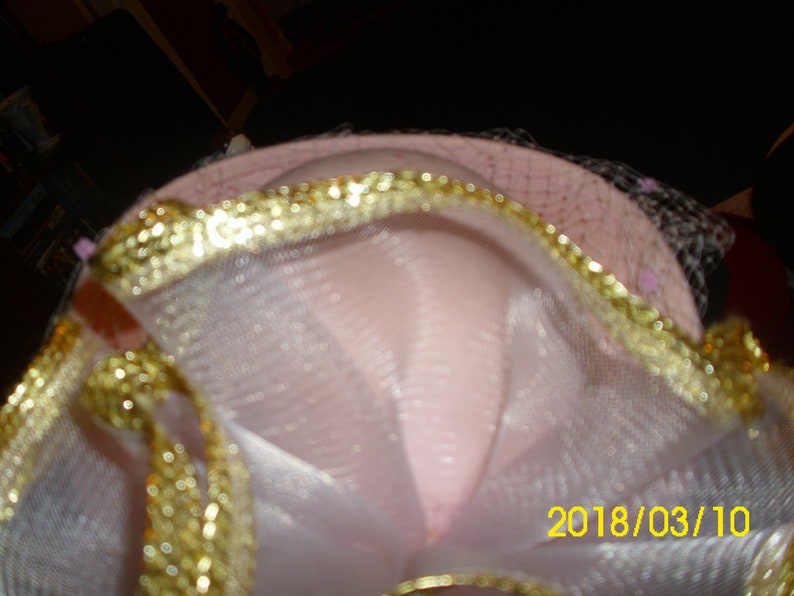 May include: A pink hat with a gold trim and white tulle. The hat has a date, 2018/03/10, written on it.