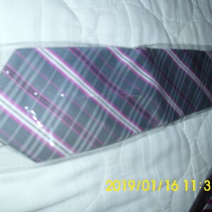 May include: A gray and pink plaid tie with a white stripe. The tie is wrapped in plastic and is lying on a white surface.