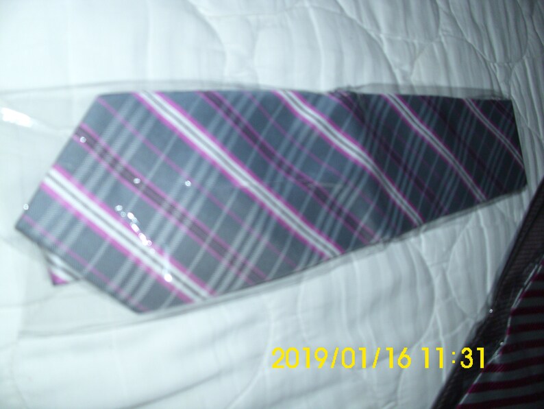 May include: A gray and pink plaid tie with a white stripe. The tie is wrapped in plastic and is lying on a white surface.