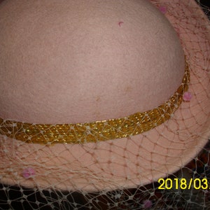 May include: A pink felt hat with a gold trim and a sheer veil. The veil has pink beads around the edge. The date 2018/03/10 is written on the bottom right corner of the image.