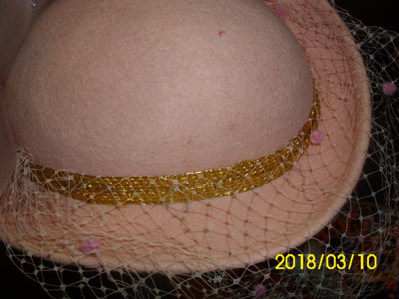 May include: A pink felt hat with a gold trim and a sheer veil. The veil has pink beads around the edge. The date 2018/03/10 is written on the bottom right corner of the image.