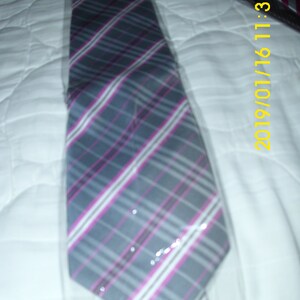 May include: A gray and pink plaid tie with a white background. The tie is folded and placed on a white surface.