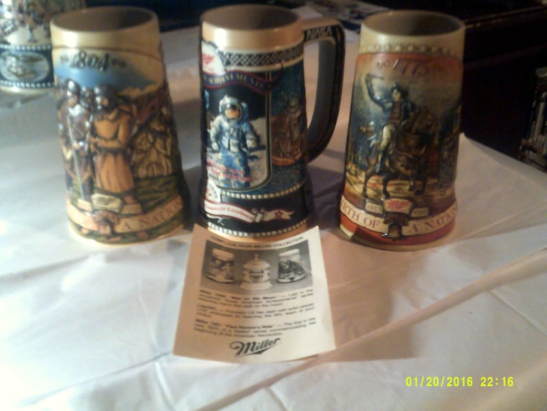 May include: Three ceramic beer steins with colorful illustrations depicting historical events. The steins feature the text "1804", "1776", and "A Nation's Birth".