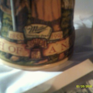 May include: A brown ceramic stein with a green, brown, and white design. The stein features a Miller Brewing Company logo and the text "1855 The Birth of a Legend 1995".