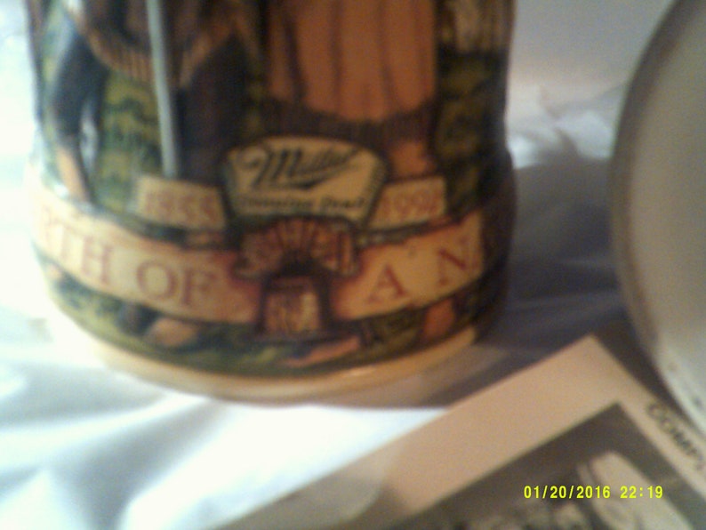 May include: A brown ceramic stein with a green, brown, and white design. The stein features a Miller Brewing Company logo and the text "1855 The Birth of a Legend 1995".