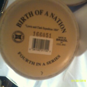 May include: A beige ceramic mug with the text "Birth of a Nation" and "Fourth in a Series" printed on the bottom. The mug also has a barcode and the text "Made in Brazil" printed on the bottom.