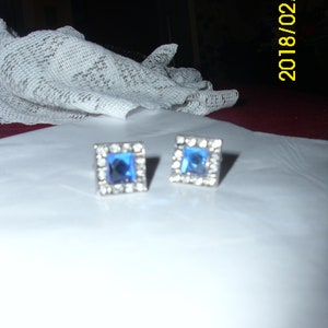 May include: A pair of silver earrings with blue square-shaped stones set in a silver frame.