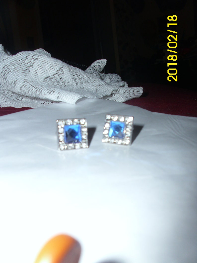 May include: A pair of silver earrings with blue square-shaped stones set in a silver frame.