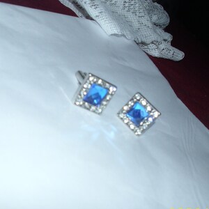 May include: A pair of silver cufflinks with blue square-shaped gemstones set in a silver frame.