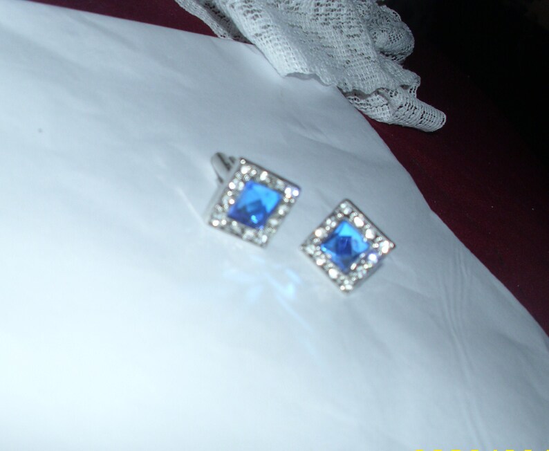 May include: A pair of silver cufflinks with blue square-shaped gemstones set in a silver frame.