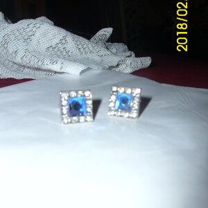 May include: A pair of silver earrings with blue square-shaped stones set in a silver frame.