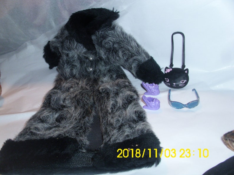 May include: A black and gray faux fur coat with a black collar and cuffs. The coat is paired with a black purse with a cat face design, purple shoes, and blue sunglasses.