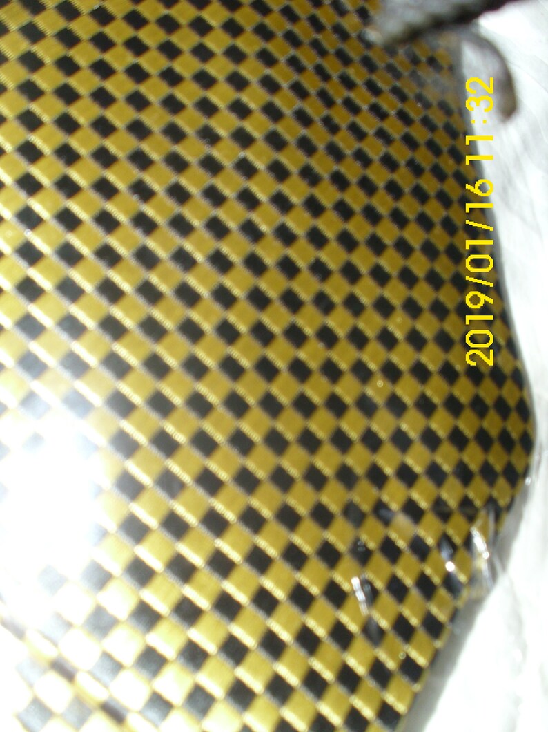 May include: A close-up of a gold and black checkered pattern. The pattern is made up of small squares. The image is slightly blurry.