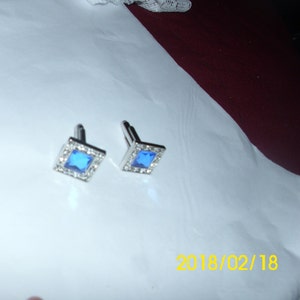 May include: A pair of silver cufflinks with blue square-shaped gemstones set in a silver frame.