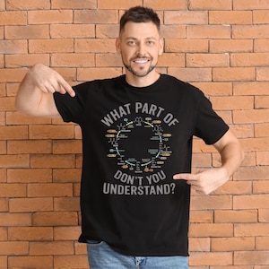 May include: Black t-shirt with the text "WHAT PART OF DON'T YOU UNDERSTAND?" in white and gray. The shirt features a diagram of a biochemical cycle in a circular design. The person is pointing at the shirt.