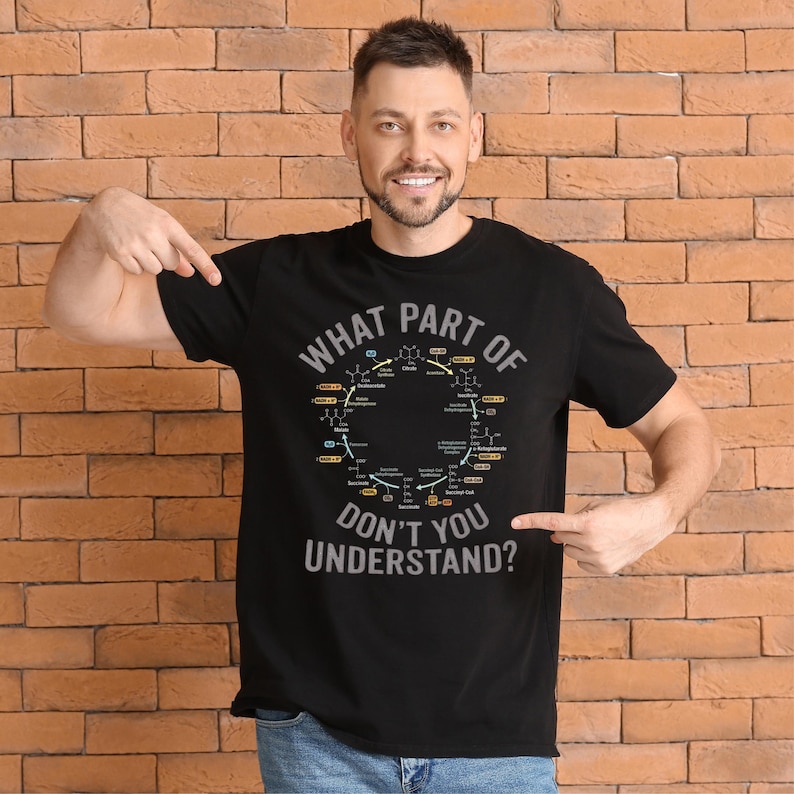 May include: Black t-shirt with the text "WHAT PART OF DON'T YOU UNDERSTAND?" in white and gray. The shirt features a diagram of a biochemical cycle in a circular design. The person is pointing at the shirt.
