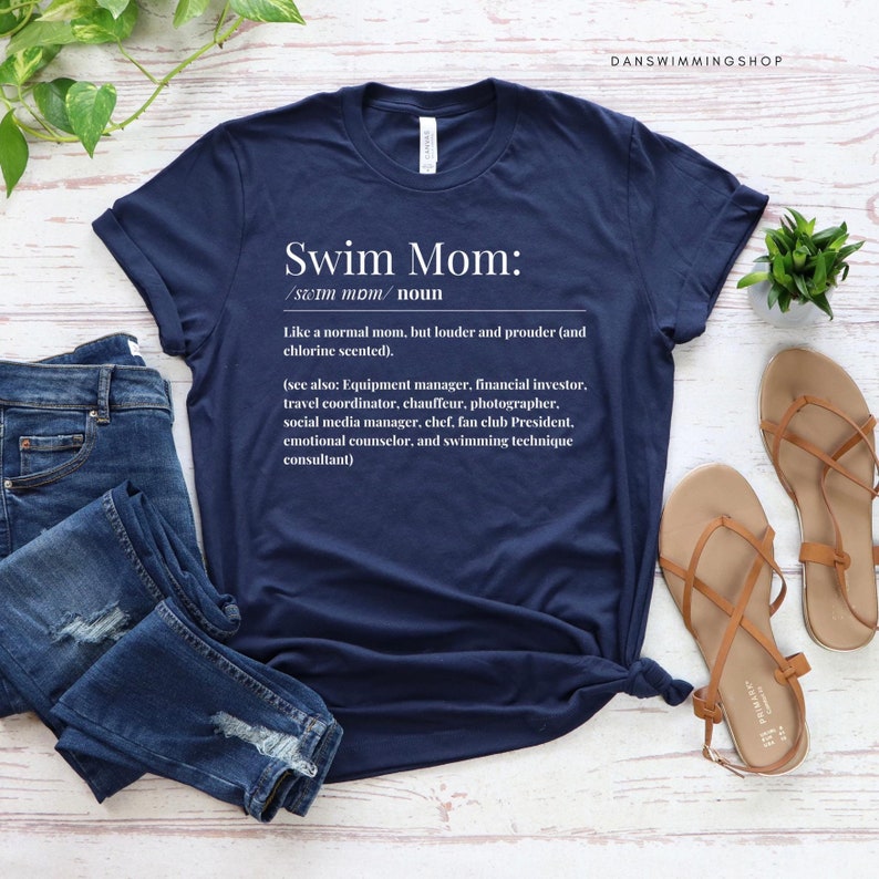 May include: A navy blue t-shirt with white text that reads "Swim Mom: /swim mom/ noun Like a normal mom, but louder and prouder (and chlorine scented). (see also: Equipment manager, financial investor, travel coordinator, chauffeur, photographer, social media manager, chef, fan club President, emotional counselor, and swimming technique consultant)"