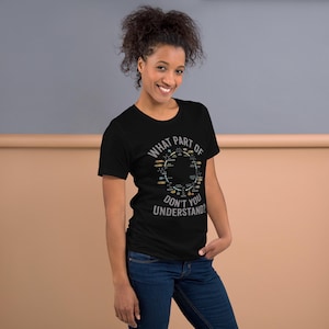 May include: Black t-shirt with the text "WHAT PART OF DON'T YOU UNDERSTAND?" in white and gray. The shirt features a circular graphic with various scientific symbols in yellow, green, and orange. The model is wearing blue jeans.