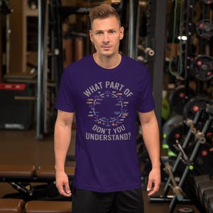 May include: A short-sleeved, dark purple t-shirt with the text "WHAT PART OF DON'T YOU UNDERSTAND?" in white and a diagram. The diagram is a circular design with various scientific symbols and labels. The shirt is made of a soft material.