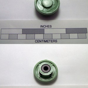 May include: A green plastic knob with a small hole in the center. The knob has a textured surface and is about 1 inch in diameter.