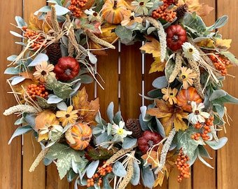 May include: A fall-themed wreath with a variety of autumnal elements, including faux pumpkins, leaves, berries, and flowers. The wreath is made with a base of green foliage and has a rustic, natural look.