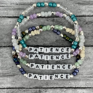 May include: Four layered beaded bracelets with the word "PATIENCE" spelled out in white letter beads on each bracelet. The bracelets are made with various colors of beads, including teal, lavender, cream, and silver.
