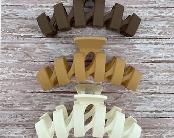 May include: Three plastic hair claw clips in different colors: brown, beige, and white. The clips are designed with a wavy, interlocking pattern.