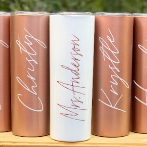 May include: Five personalized tumblers with rose gold and white finishes. The tumblers are labeled with the names "Lindsay", "Christy", "Mrs. Anderson", "Krystle", and "Heidi".
