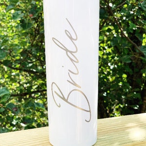 May include: White stainless steel tumbler with the word "Bride" engraved in a cursive font.