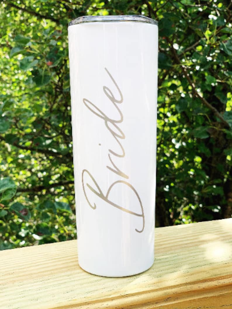 May include: White stainless steel tumbler with the word "Bride" engraved in a cursive font.