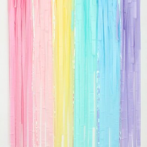 May include: Rainbow colored tissue paper streamers hanging from a white wall. The streamers are in shades of pink, yellow, blue, and purple.
