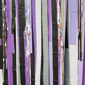 May include: A wall decorated with strips of purple, black, silver, and white paper streamers.