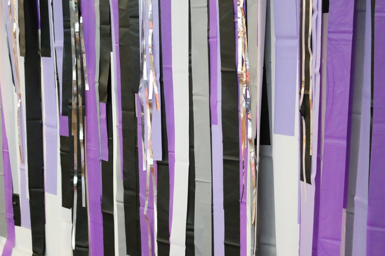 May include: A wall decorated with strips of purple, black, silver, and white paper streamers.