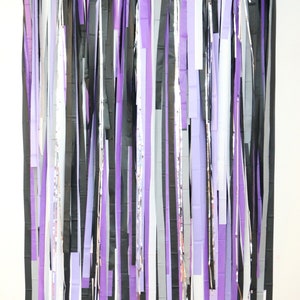 May include: A backdrop made of purple, black, and white streamers hanging from a string. The streamers are all different lengths and are arranged in a random pattern.