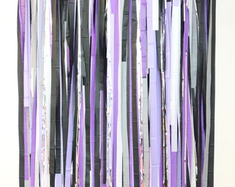 May include: A backdrop made of purple, black and white streamers hanging from a string. The streamers are all different lengths and are arranged in a random pattern.