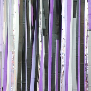 May include: A wall decorated with a curtain of purple, black, and silver streamers. The streamers are hanging from the ceiling and are arranged in a random pattern.