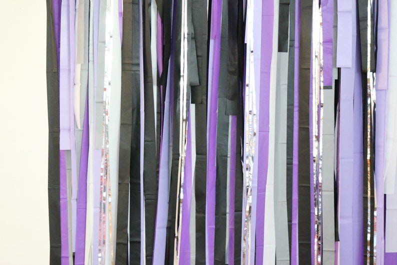 May include: A wall decorated with a curtain of purple, black, and silver streamers. The streamers are hanging from the ceiling and are arranged in a random pattern.
