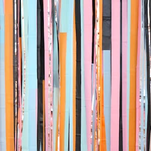 May include: A colorful backdrop of streamers in various colors, including black, orange, pink, blue, and silver. The streamers are hanging vertically and create a festive and celebratory atmosphere.