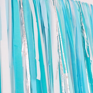 May include: A backdrop of blue and white streamers with silver accents. The streamers are hanging vertically and are made of a lightweight material.